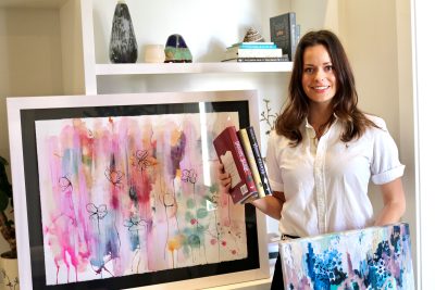 Mary Beesley stands with her paintings and published books, St. George, Utah, June 26, 2022 | Photo by Jessi Bang, St. George News