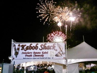 The Kabob Shack booth is lit up as fireworks are seen overhead, location and date unspecified | Photo courtesy of Stacia Mizukawa