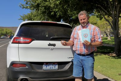Paul Zolman, owner of Role of Love, takes a photo with his custom license plate, dice, books and journal, St. George, Utah, Sept. 25, 2023 | Photo by Jessi Bang, St. George News