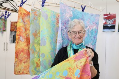 Artist Lynda Holman stands with her silk marbling designs at her home studio in St. George, Utah, Nov. 30, 2023 | Photo by Jessi Bang, St. George News